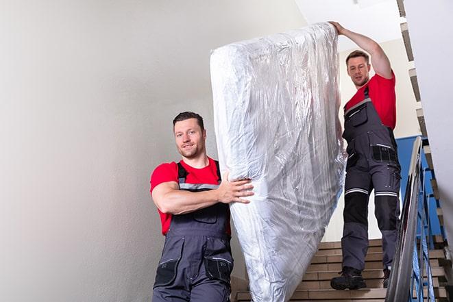 workers maneuvering a box spring through a narrow hallway in Manville, RI